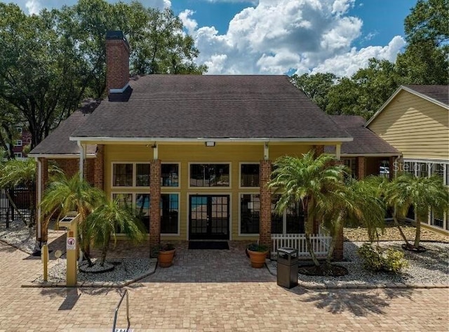 back of house with french doors, a chimney, and a shingled roof
