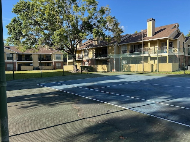 view of tennis court with community basketball court, fence, and a residential view