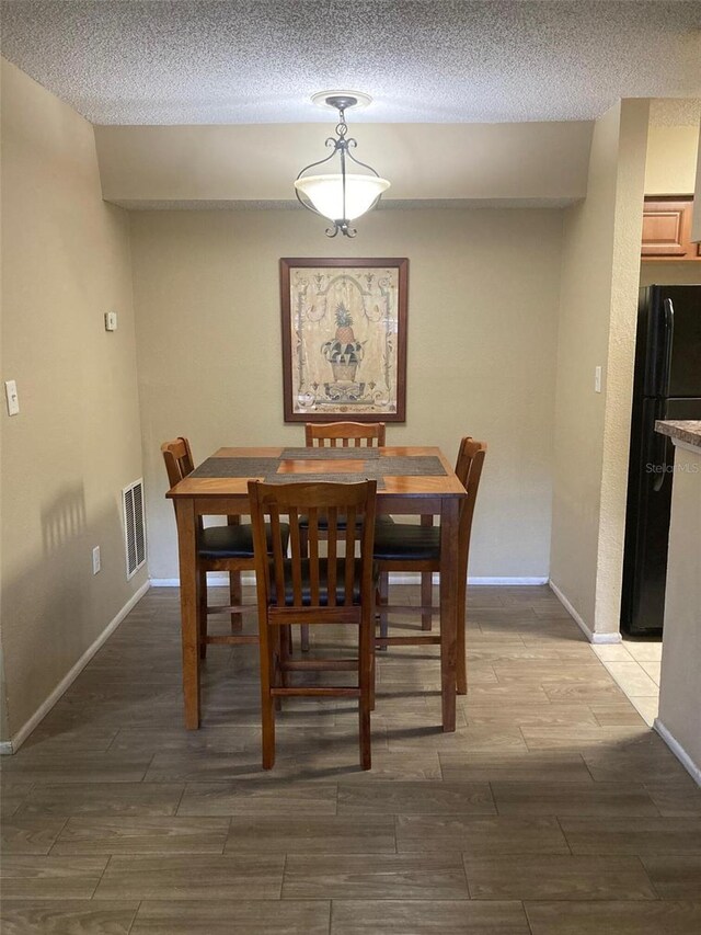 dining area featuring visible vents, baseboards, wood finish floors, and a textured ceiling