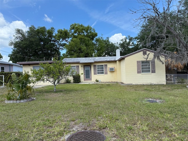ranch-style home with a wall mounted AC, fence, a chimney, a front yard, and concrete block siding