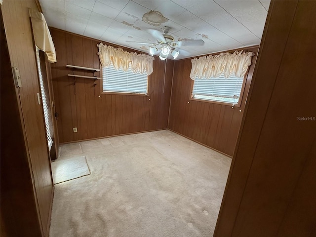 unfurnished bedroom with light colored carpet, wooden walls, multiple windows, and a ceiling fan