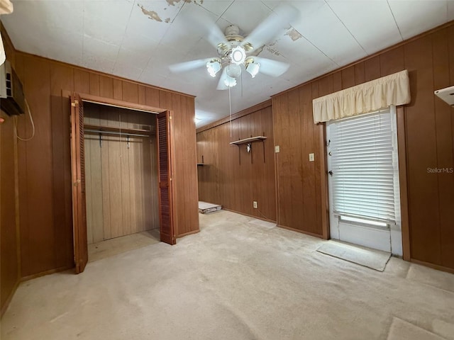 unfurnished bedroom featuring a ceiling fan, light carpet, a closet, and wooden walls