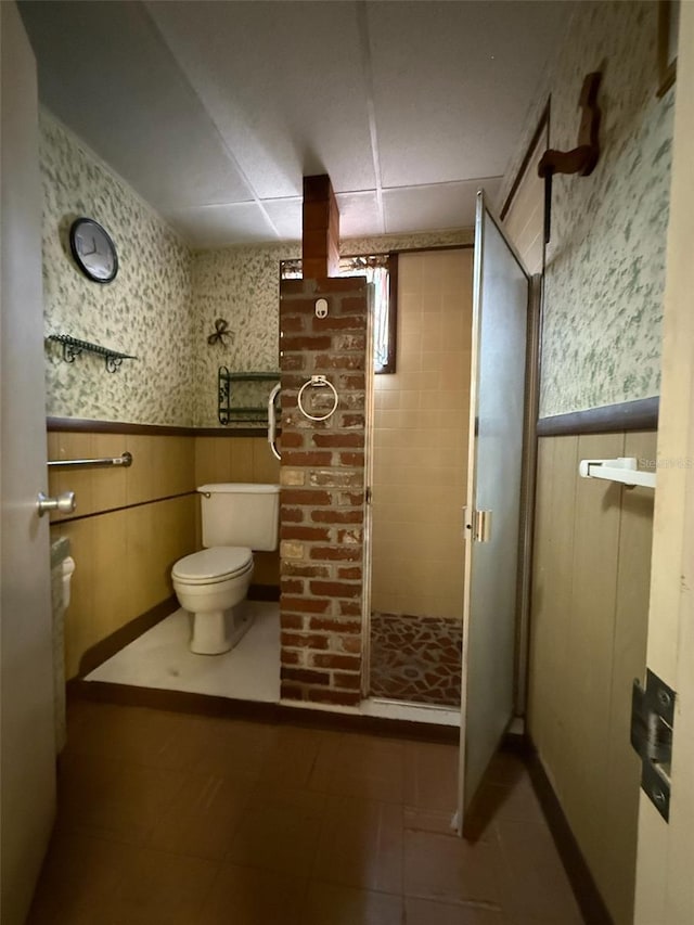 full bath featuring a wainscoted wall, toilet, a shower stall, and wallpapered walls