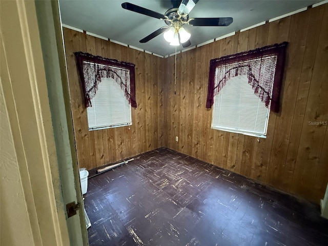 spare room featuring ceiling fan, dark floors, and wooden walls