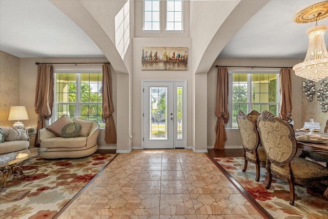 foyer entrance featuring arched walkways, stone finish floor, baseboards, and a towering ceiling
