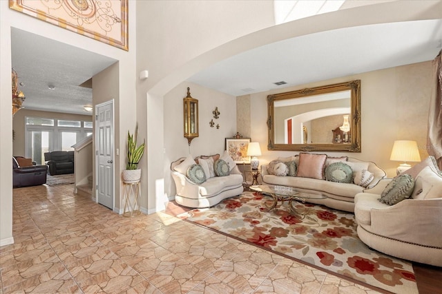 living area featuring arched walkways, stone finish floor, visible vents, and baseboards