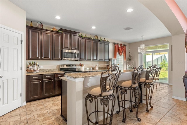 kitchen featuring light stone countertops, arched walkways, a breakfast bar, a kitchen island with sink, and stainless steel appliances
