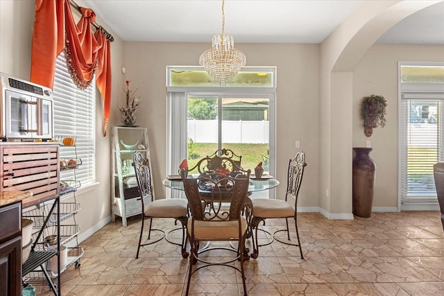 dining space featuring baseboards, stone finish floor, arched walkways, and a notable chandelier