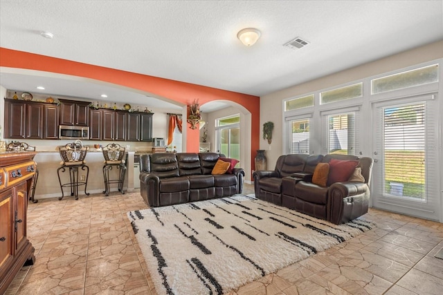 living area with arched walkways, a textured ceiling, stone finish flooring, recessed lighting, and visible vents