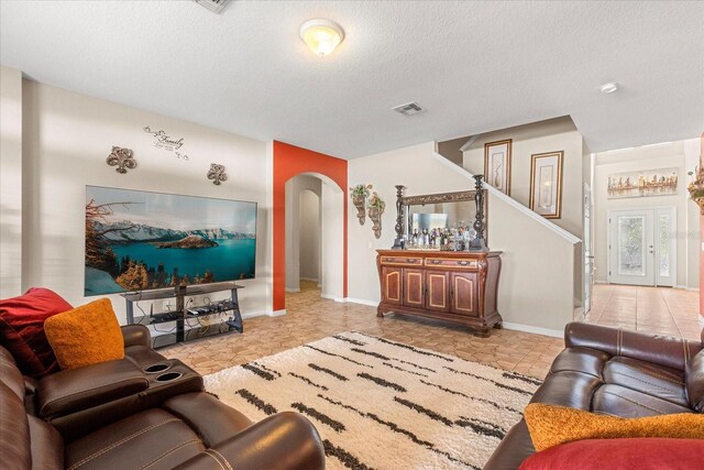 living room featuring baseboards, stairway, a textured ceiling, visible vents, and arched walkways