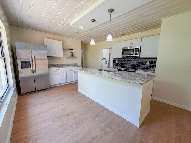 kitchen with a sink, light stone countertops, appliances with stainless steel finishes, light wood-style flooring, and decorative backsplash