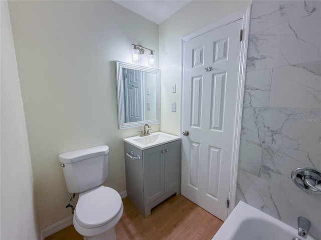 bathroom with washtub / shower combination, baseboards, wood finished floors, toilet, and vanity