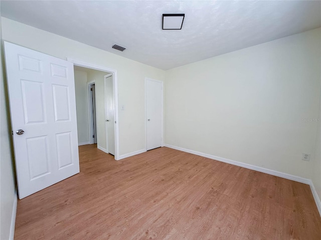 empty room featuring light wood finished floors, baseboards, and visible vents