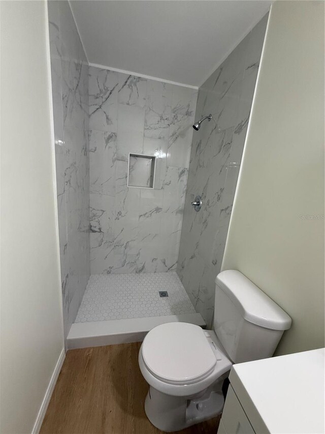 bathroom with toilet, wood finished floors, and a marble finish shower