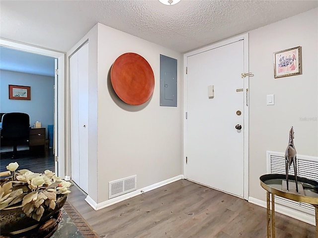 foyer with electric panel, wood finished floors, baseboards, and a textured ceiling