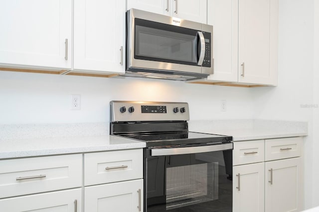 kitchen with light stone counters, appliances with stainless steel finishes, and white cabinetry