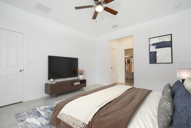 tiled bedroom with a spacious closet, visible vents, and ceiling fan