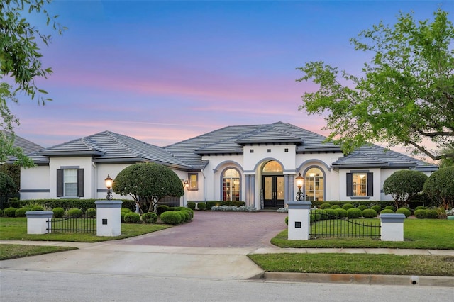 view of front facade with french doors, decorative driveway, stucco siding, and a fenced front yard