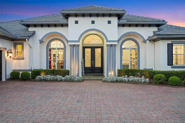 property entrance featuring french doors, driveway, stucco siding, and a tiled roof