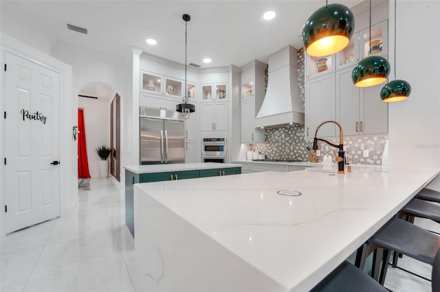 kitchen featuring custom exhaust hood, visible vents, arched walkways, appliances with stainless steel finishes, and backsplash