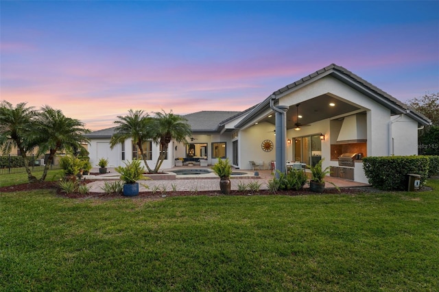 back of house at dusk featuring a lawn, a patio, an in ground hot tub, and area for grilling