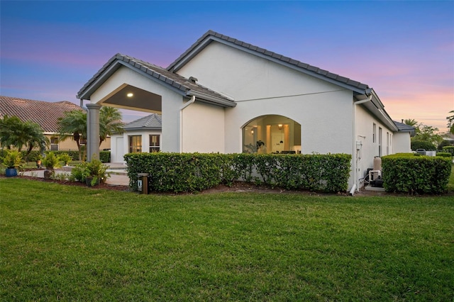 back of property at dusk featuring a yard, stucco siding, and a tiled roof
