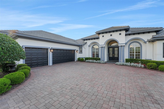mediterranean / spanish-style house featuring french doors, a garage, stucco siding, and decorative driveway