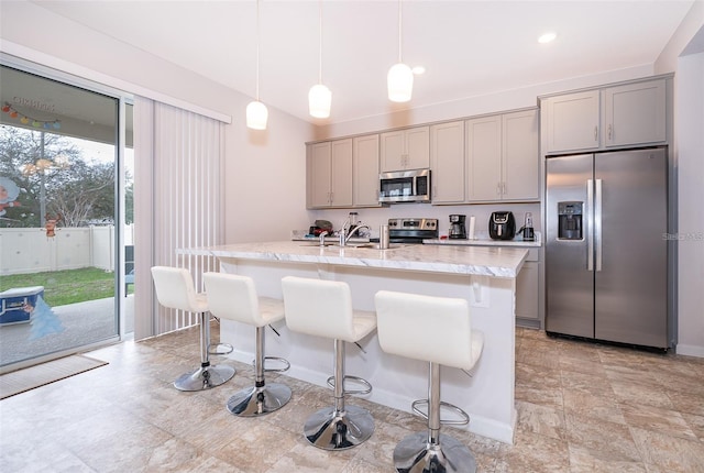 kitchen with a kitchen breakfast bar, gray cabinets, a center island with sink, appliances with stainless steel finishes, and a sink