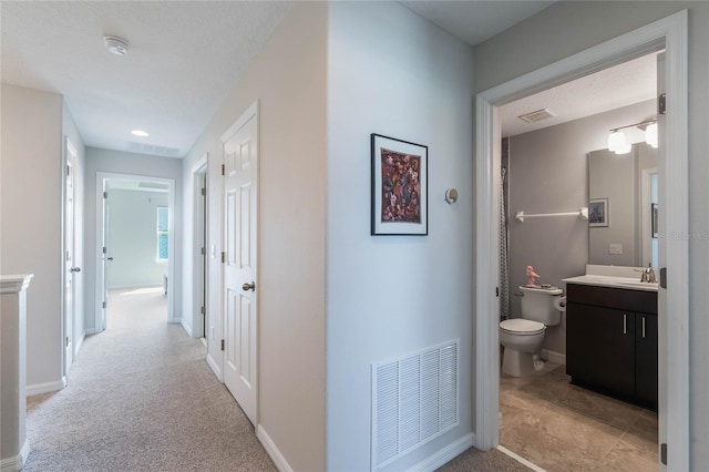 hall featuring light colored carpet, baseboards, and visible vents