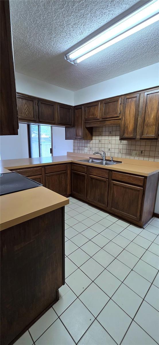 6277 Cranberry Ln W, Jacksonville, FL 32244 - kitchen with dark brown cabinets, a sink, a textured ceiling, backsplash, and light tile patterned floors