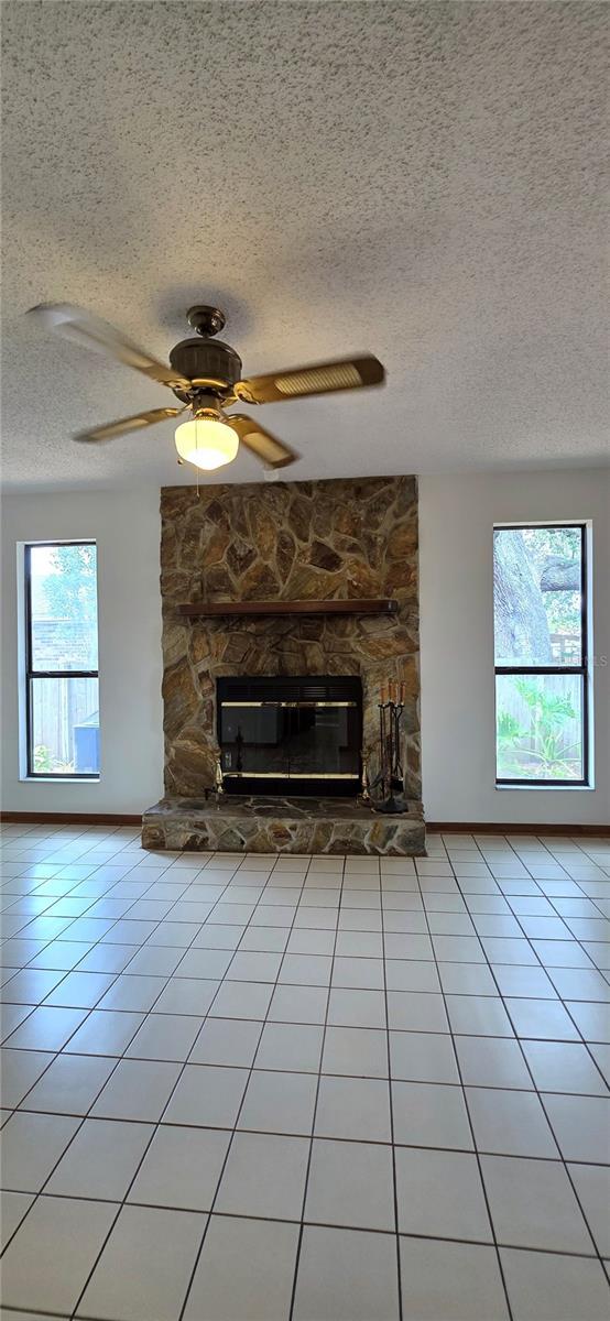 6277 Cranberry Ln W, Jacksonville, FL 32244 - unfurnished living room featuring a fireplace, a textured ceiling, light tile patterned floors, ceiling fan, and baseboards