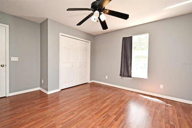 unfurnished bedroom with a closet, baseboards, ceiling fan, and wood finished floors