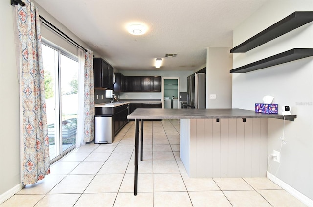 kitchen featuring a peninsula, light tile patterned floors, and freestanding refrigerator