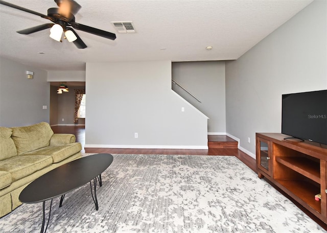 living room with ceiling fan, visible vents, wood finished floors, stairs, and baseboards