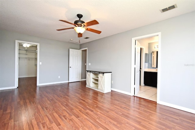 unfurnished bedroom with visible vents, baseboards, a textured ceiling, a walk in closet, and wood finished floors