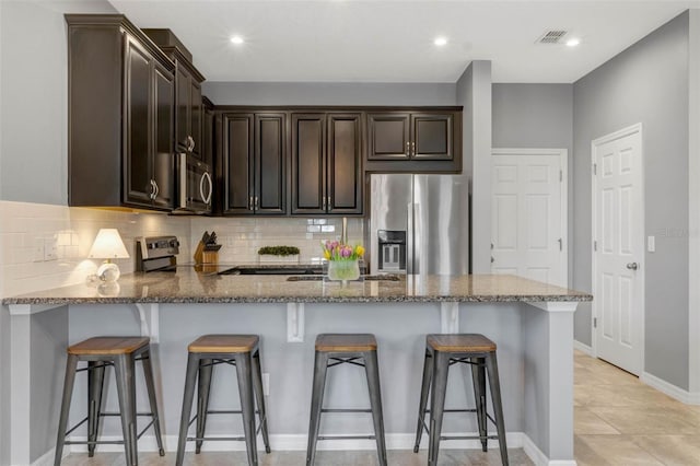 9433 Randal Park Blvd, Orlando, FL 32832 - kitchen with stone countertops, dark brown cabinetry, a peninsula, backsplash, and appliances with stainless steel finishes
