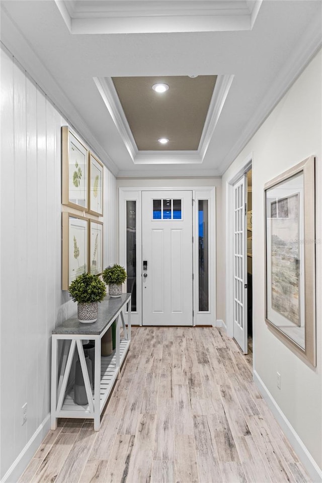 entrance foyer featuring crown molding, a raised ceiling, and light wood-style floors