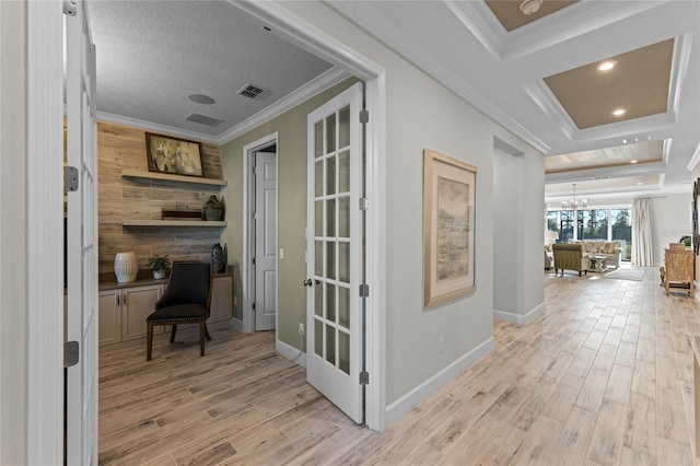 corridor with visible vents, light wood-type flooring, a chandelier, ornamental molding, and a tray ceiling