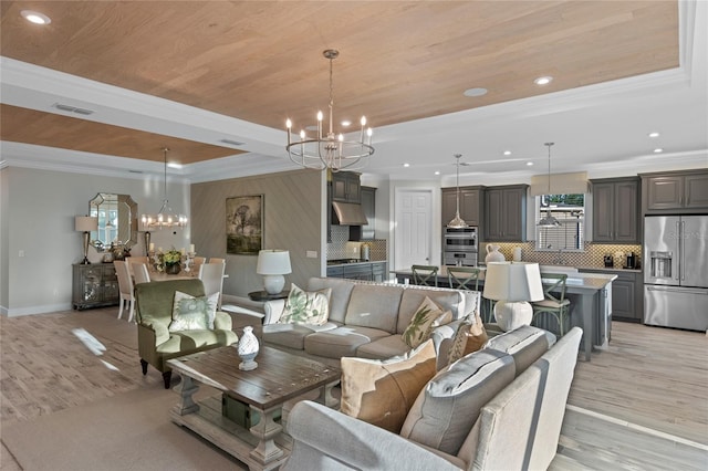 living area with a notable chandelier, ornamental molding, a raised ceiling, and light wood-type flooring