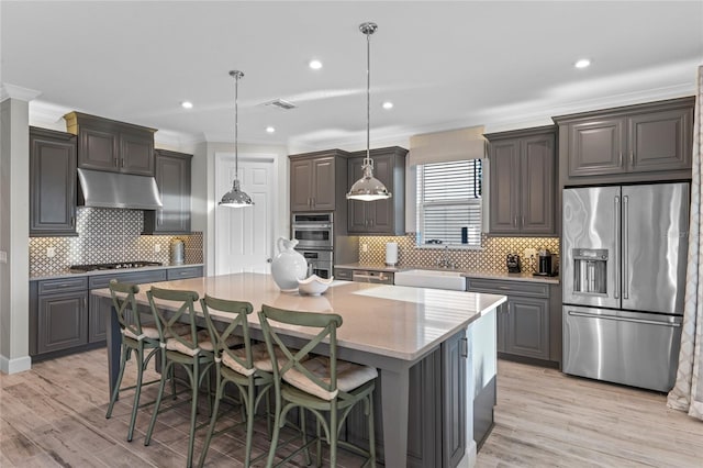 kitchen with backsplash, crown molding, appliances with stainless steel finishes, light wood-type flooring, and under cabinet range hood