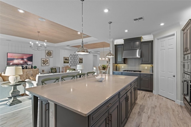 kitchen featuring visible vents, ornamental molding, a center island, light wood finished floors, and a notable chandelier