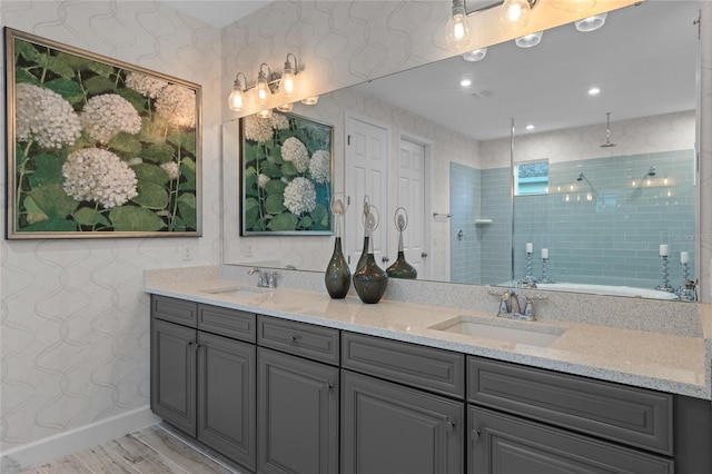 full bath with a sink, a tile shower, double vanity, and wood finished floors
