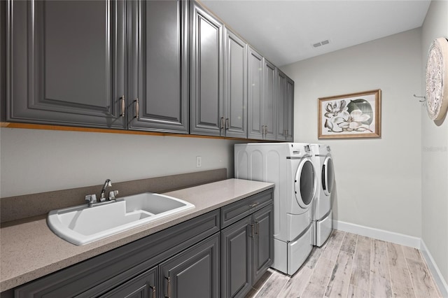 clothes washing area with cabinet space, a sink, light wood-type flooring, visible vents, and washing machine and dryer