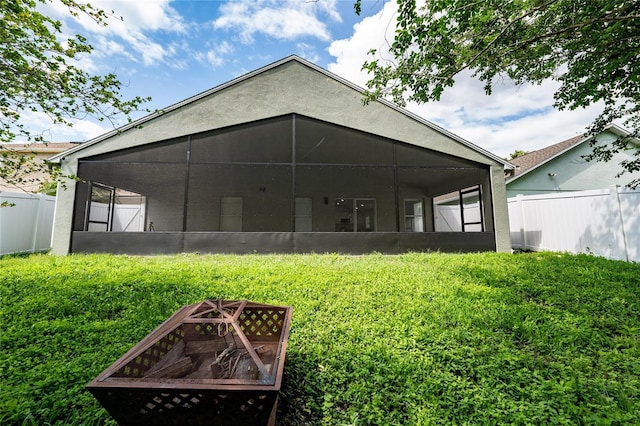 back of house with a sunroom, stucco siding, fence, and a lawn