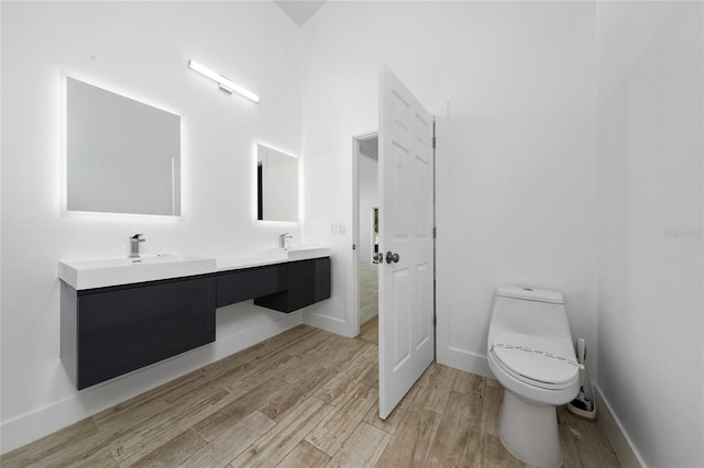 full bath featuring toilet, wood finished floors, double vanity, and a sink