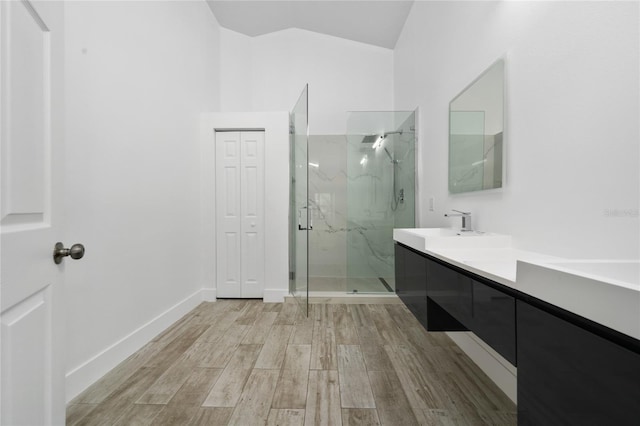 bathroom with baseboards, vanity, vaulted ceiling, wood finished floors, and a marble finish shower