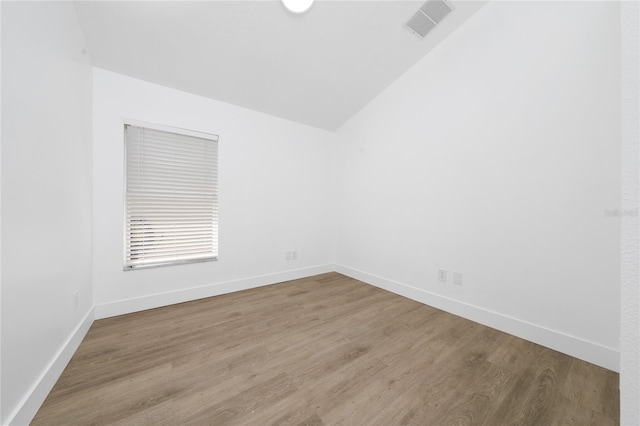 unfurnished room featuring wood finished floors, baseboards, lofted ceiling, and visible vents