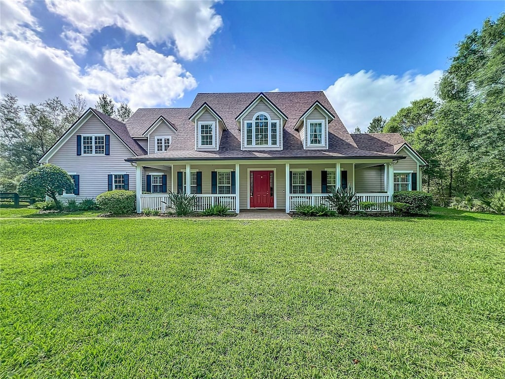 cape cod home with roof with shingles, a front lawn, and covered porch