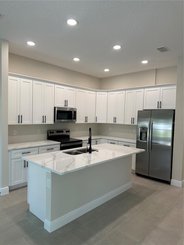 kitchen with white cabinets, a sink, visible vents, stainless steel appliances, and a kitchen island with sink