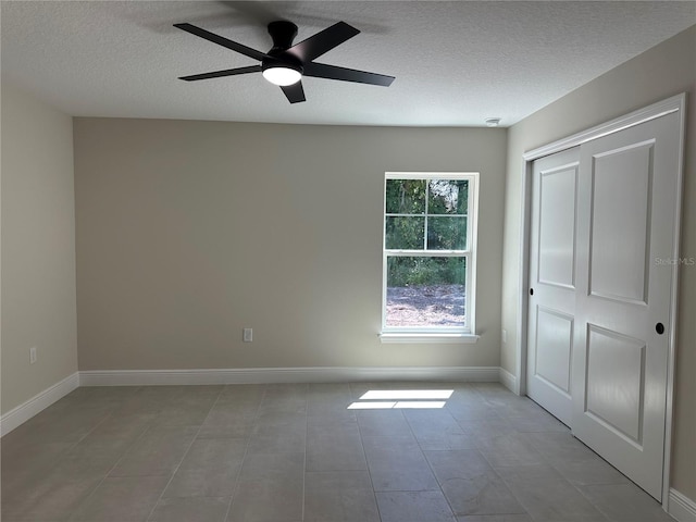unfurnished bedroom featuring a textured ceiling, ceiling fan, tile patterned flooring, and baseboards